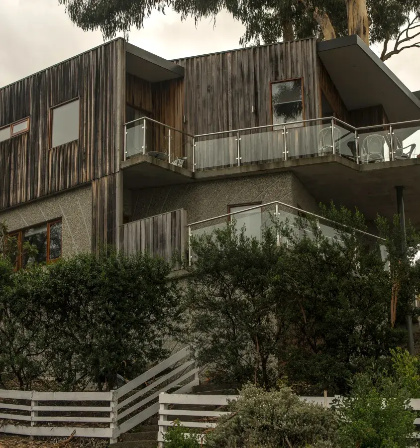 Photo of a multi-storey house in Blackman's Bay with weathered vertical timber cladding and multiple decks with glass balustrading.