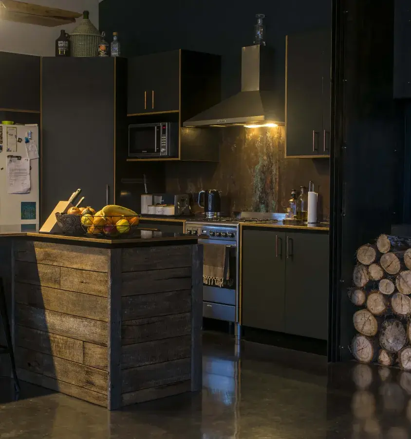 Moody lighting in modern kitchen with a polished black slab floor, rustic timber elements and rusted corten fireplace